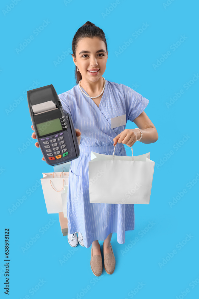 Young woman with shopping bag and payment terminal on blue background