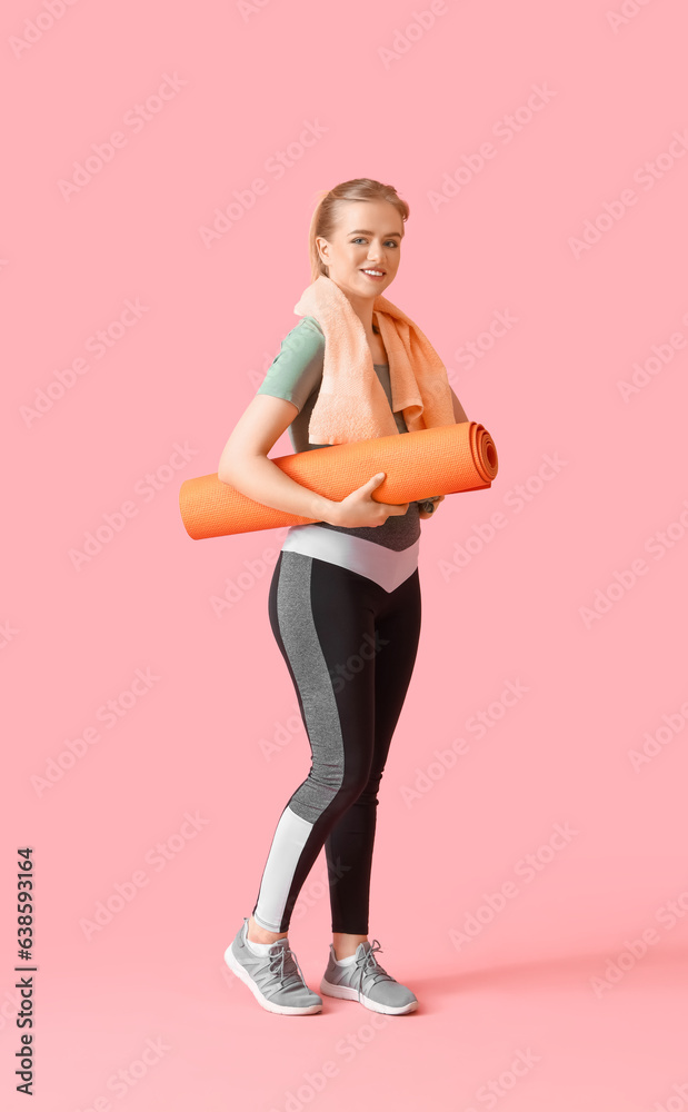 Portrait of sporty young woman with yoga mat and towel on pink background