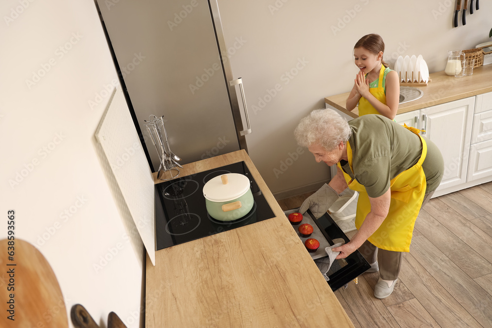 Little girl with her grandmother baking muffins in kitchen