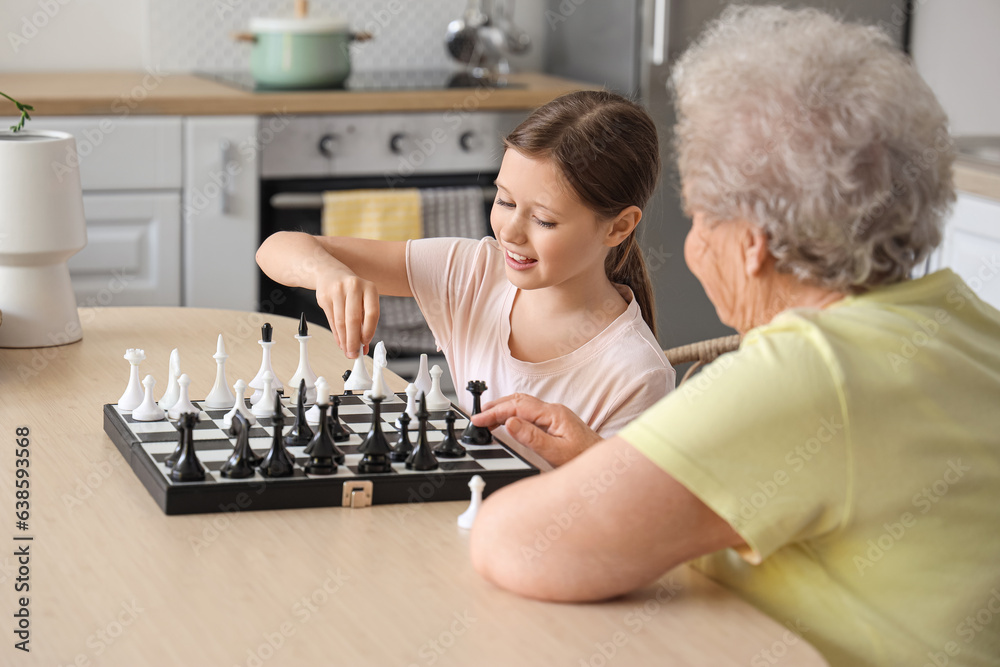 Little girl with her grandmother playing chess in kitchen