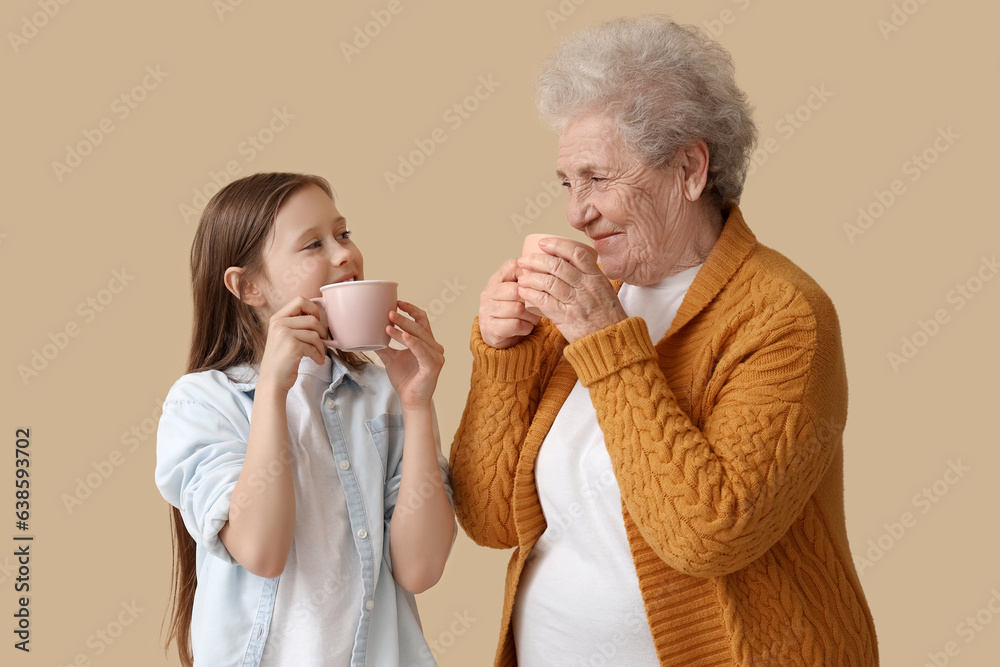 Little girl with her grandmother drinking tea on beige background