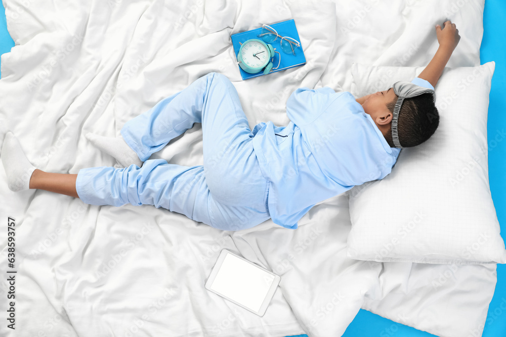 Little African-American boy with soft blanket sleeping on blue background, top view