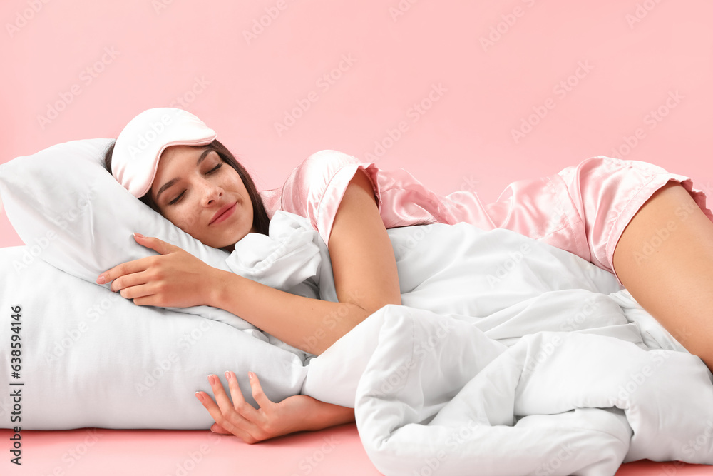 Beautiful young woman with pillow and soft blanket sleeping on pink background