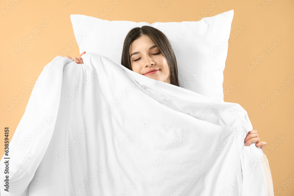 Beautiful happy young woman with pillow and soft blanket sleeping on pale orange background