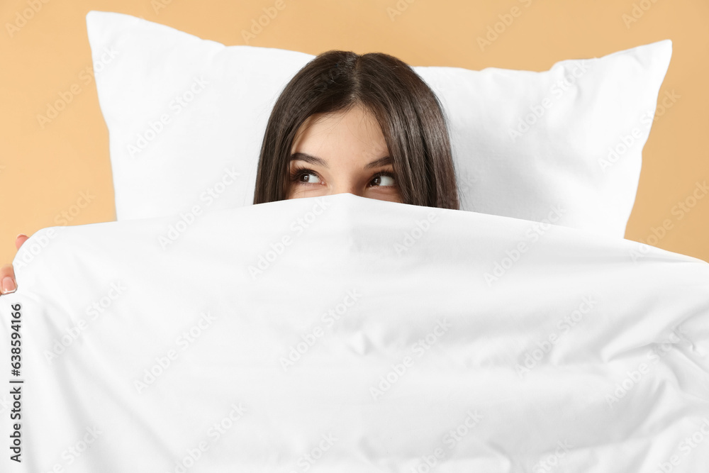 Beautiful thinking young woman with pillow and soft blanket on pale orange background