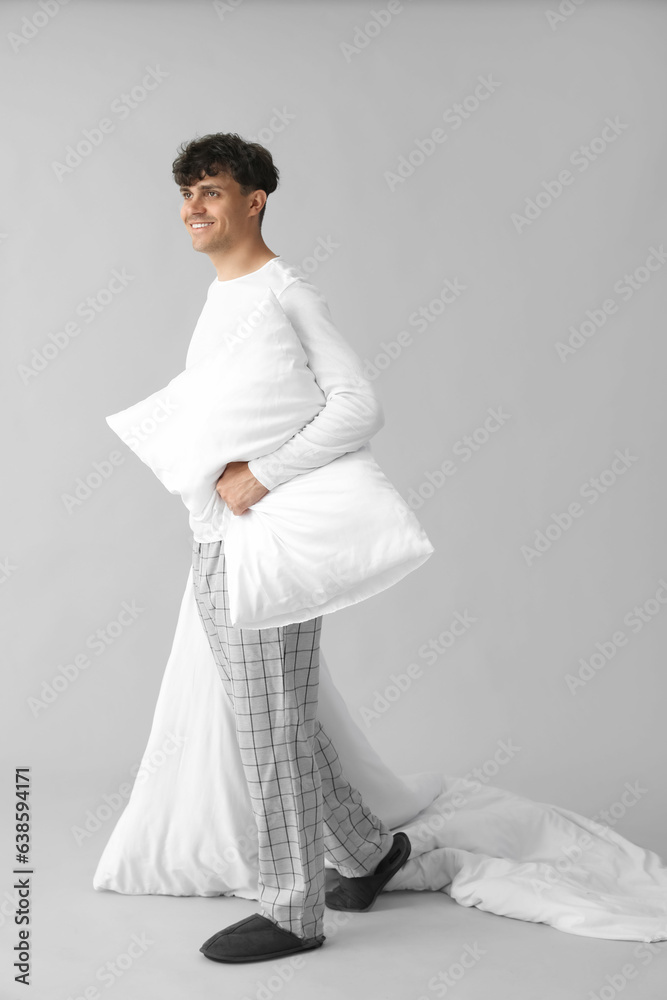 Handsome happy man with soft blanket and pillow on grey background