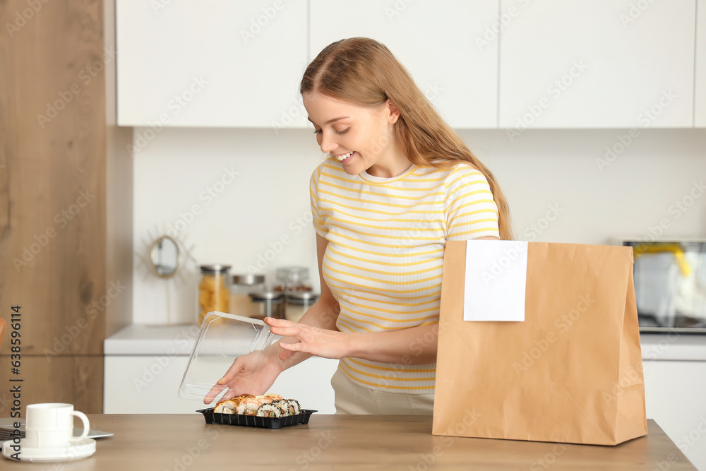 Happy young woman with sushi and paper bag in kitchen