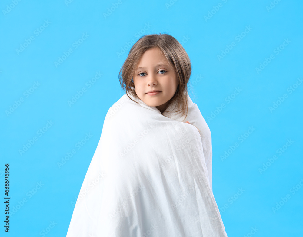 Little girl wrapped in blanket on blue background