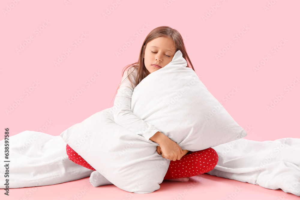 Sleepy little girl with pillow and blanket on pink background