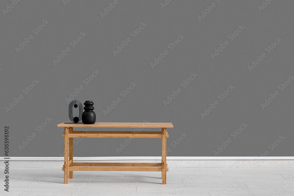 Wooden table with empty vase and decorative figure near grey wall