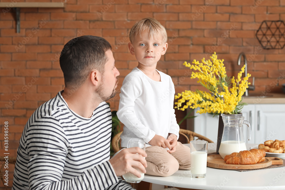 Little boy with his father sitting at table and drinking milk in kitchen