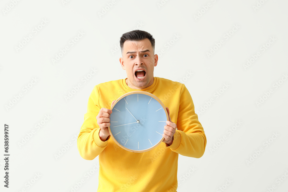 Stressed young man with clock on light background. Deadline concept