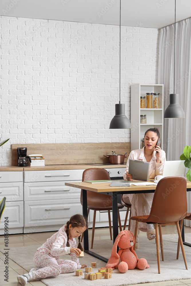 Little girl playing with cubes while her mother working in kitchen