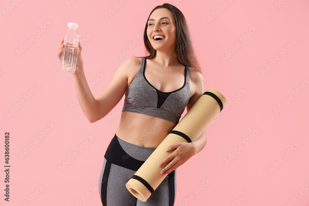 Sporty young woman with bottle of water and fitness mat on pink background