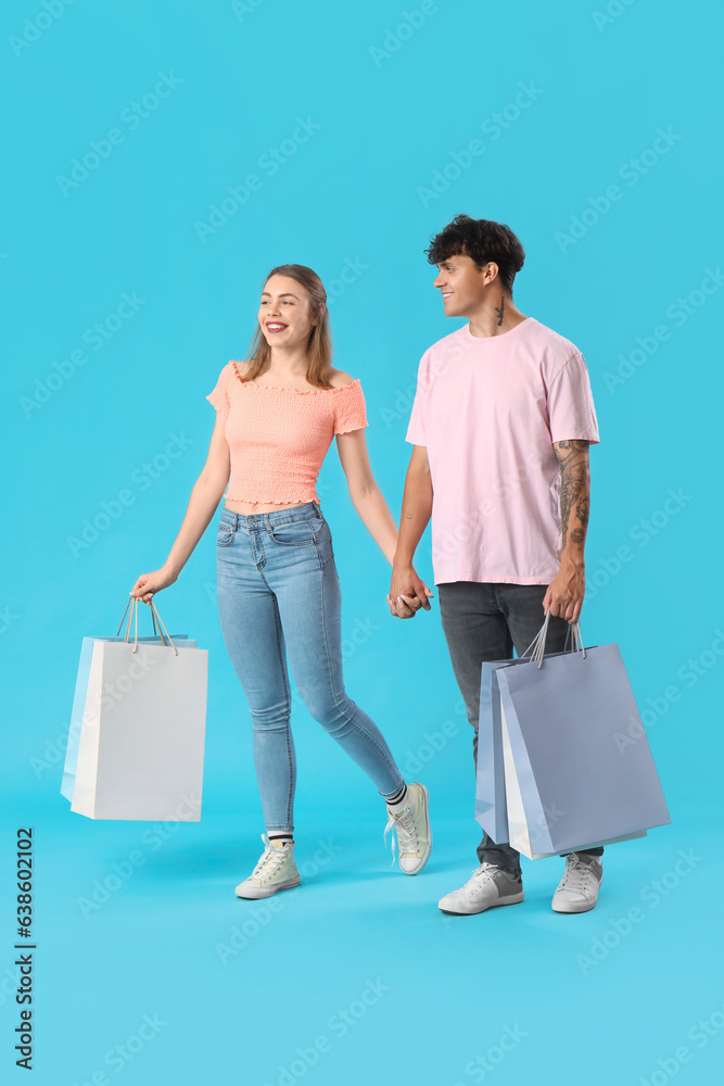 Happy young couple with shopping bags walking on blue background