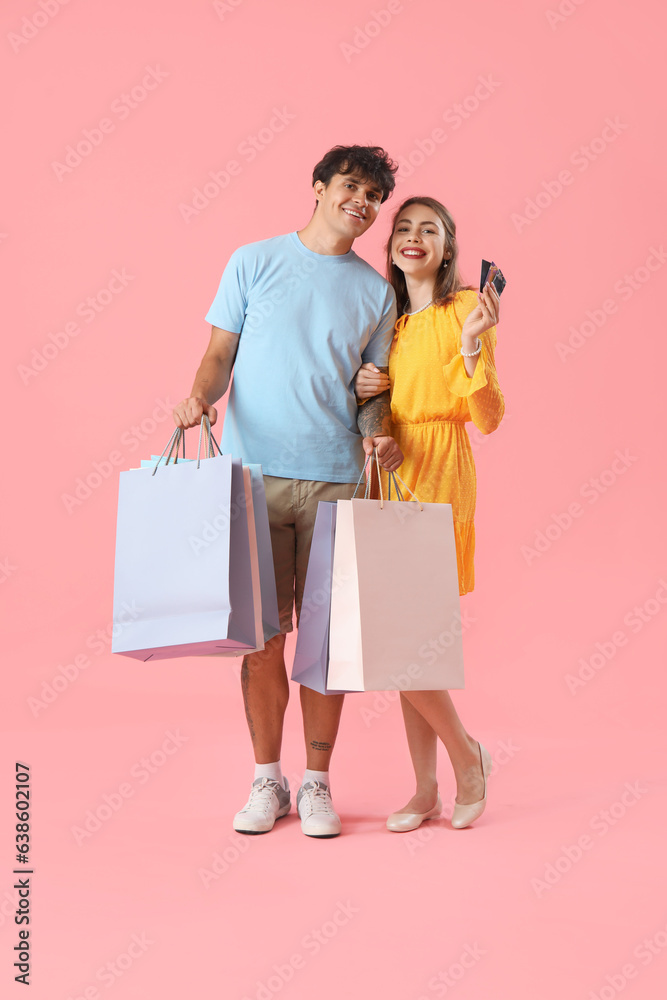 Happy young couple with credit cards and shopping bags on pink background