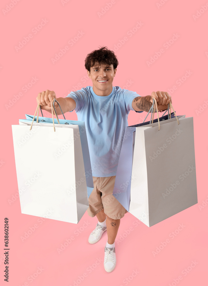 Young man with shopping bags on pink background