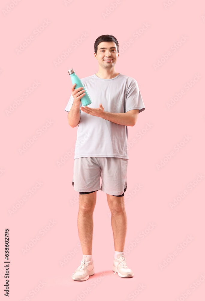 Sporty young man with bottle of water on pink background