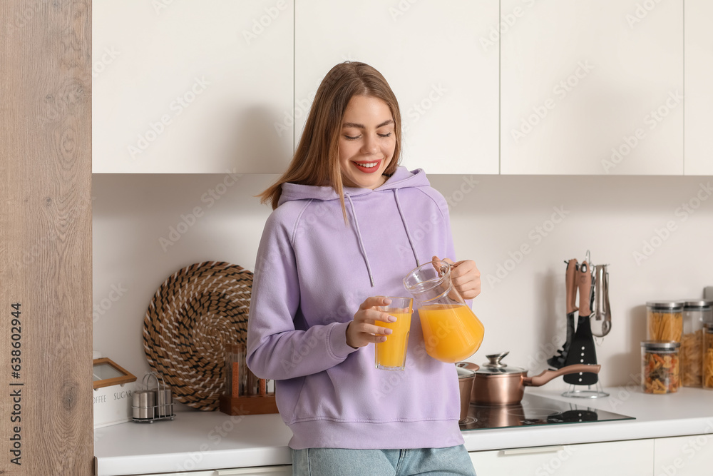 Young woman pouring orange juice into glass in kitchen