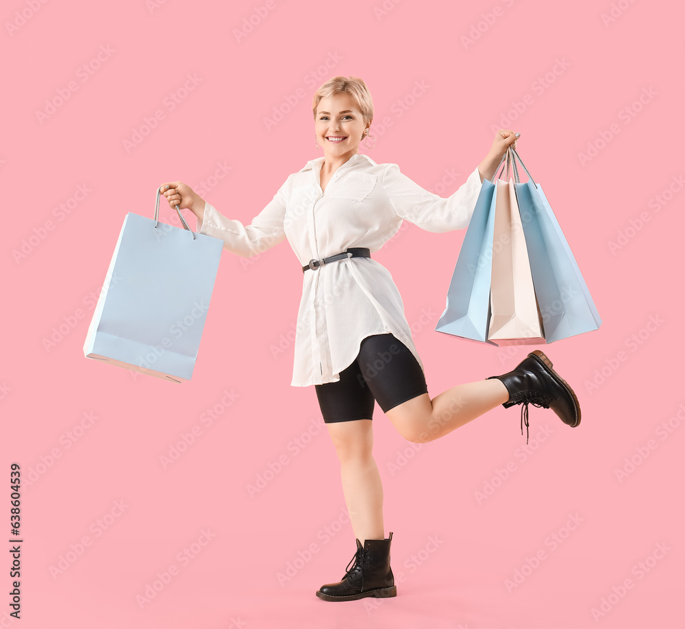 Happy beautiful young woman with shopping bags on pink background