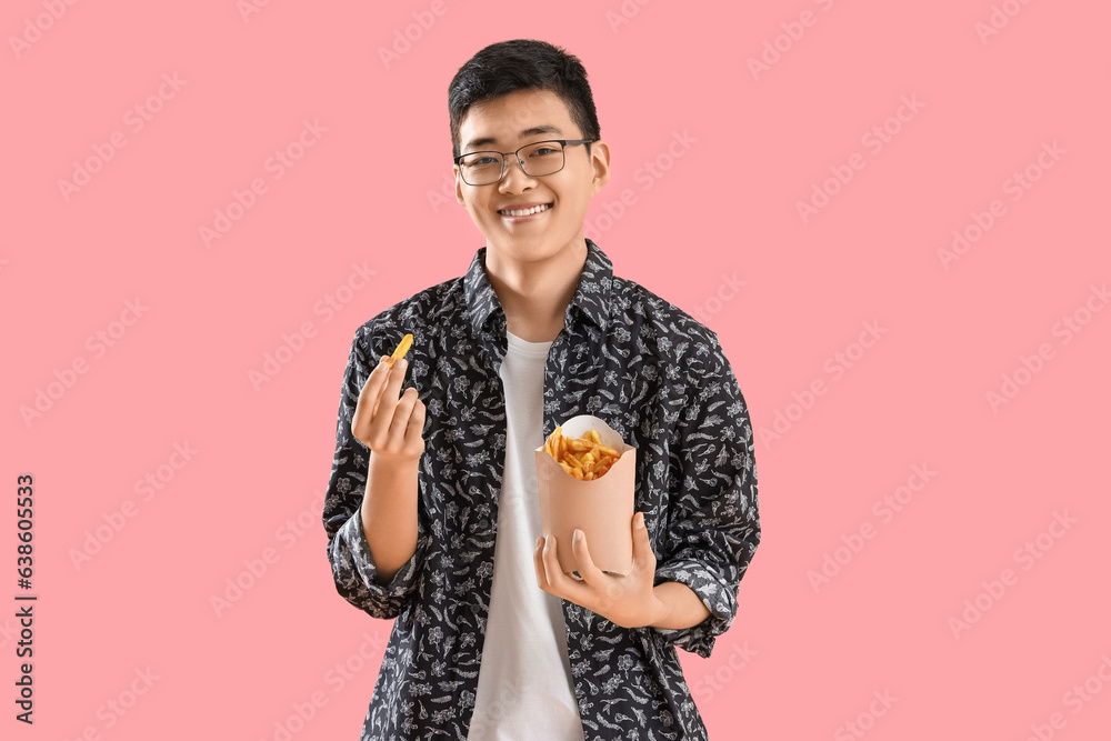 Young Asian man with french fries on pink background