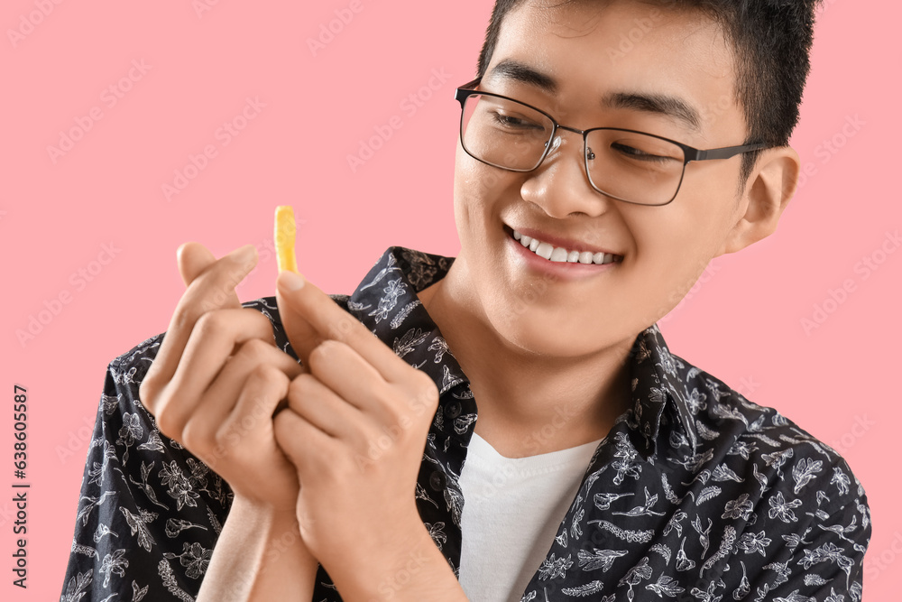 Young Asian man with french fries on pink background, closeup