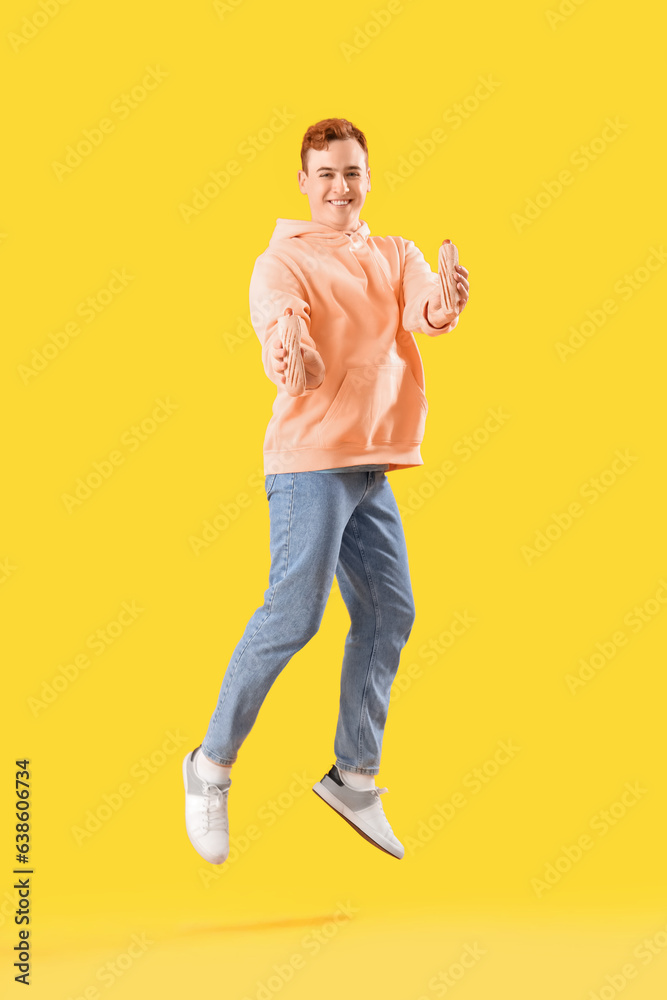 Jumping young man with tasty hot dogs on yellow background