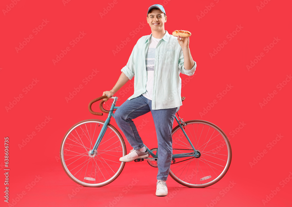 Young man with tasty hot dog and bicycle on red background