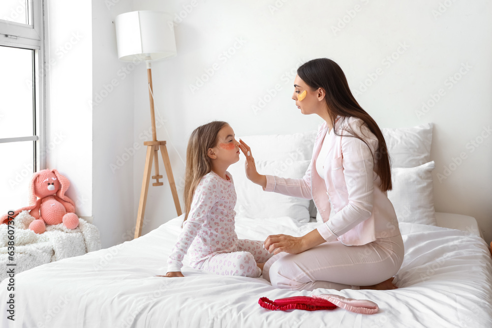 Happy mother and her little daughter with under-eye patches in bedroom