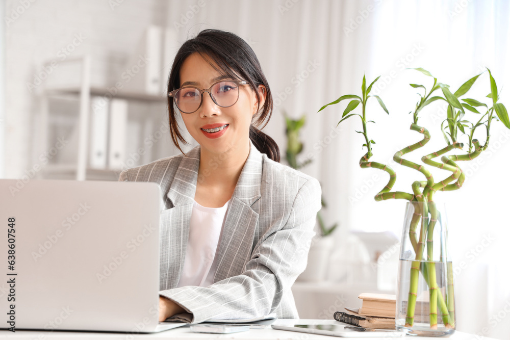 Young Asian businesswoman sitting at table and working with laptop in office