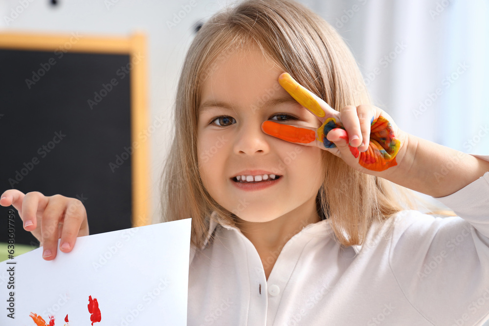 Cute little girl with her hand in paint and drawing showing victory gesture at home, closeup