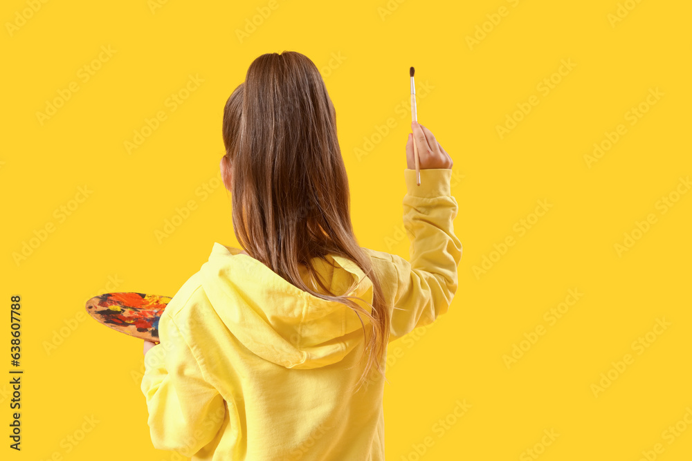 Cute little girl with paint palette and brush on yellow background, back view