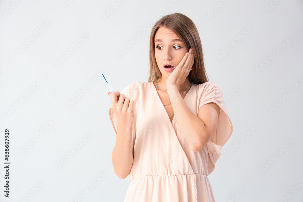 Shocked beautiful young woman with pregnancy test on grey background