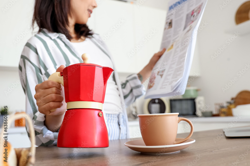 Beautiful young Asian woman with geyser coffee maker and cup of espresso reading newspaper in kitche