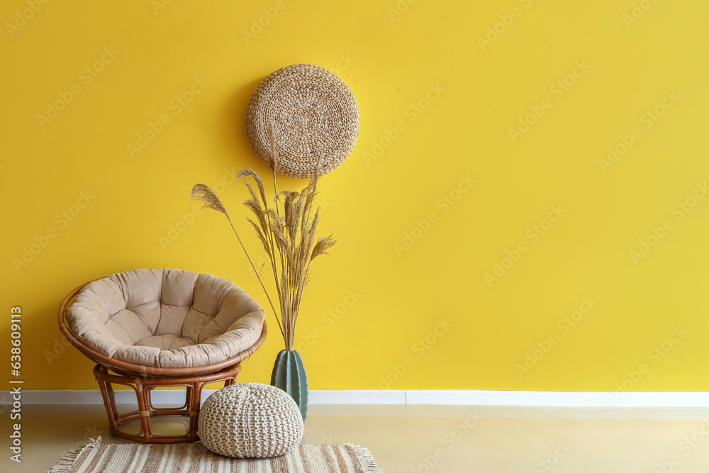 Stylish armchair, pouf and vase with pampas grass near yellow wall