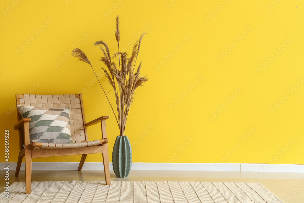 Stylish armchair and vase with pampas grass near yellow wall