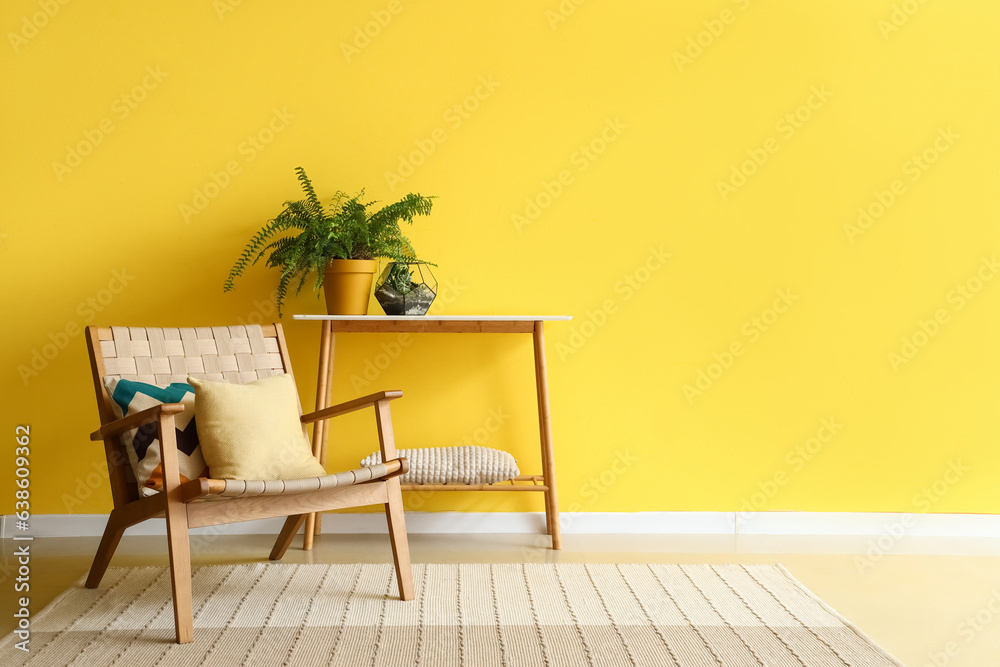 Stylish armchair and houseplant on console table near yellow wall