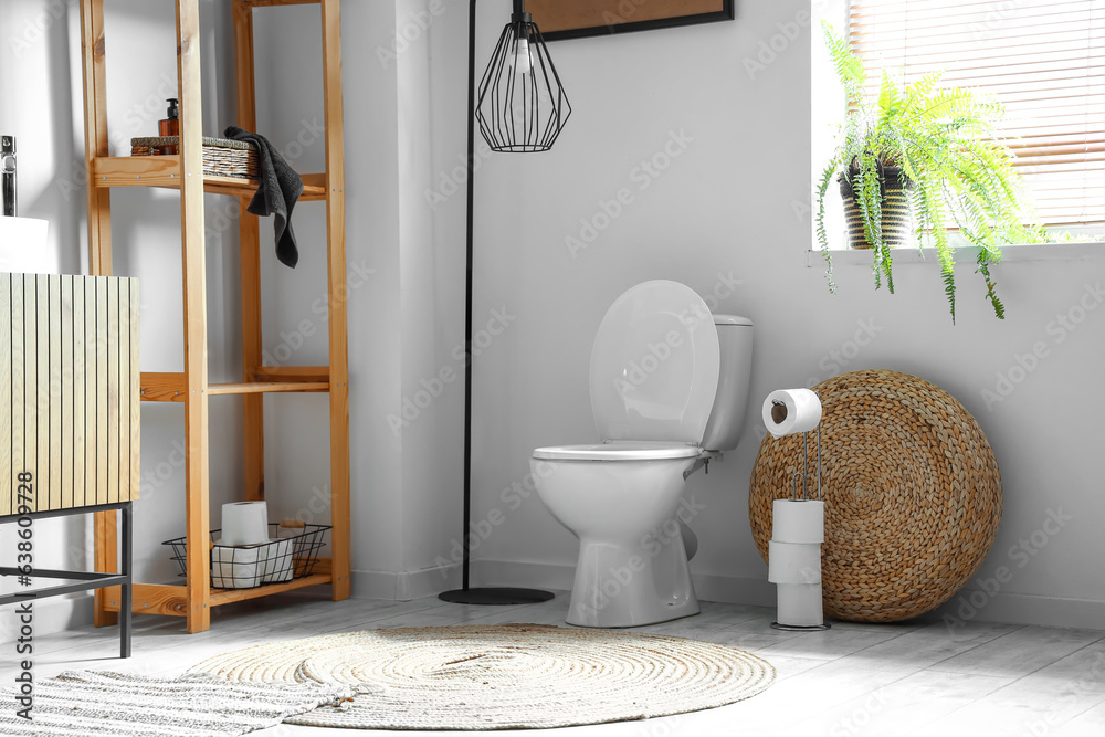 Interior of modern restroom with ceramic toilet bowl and shelving unit