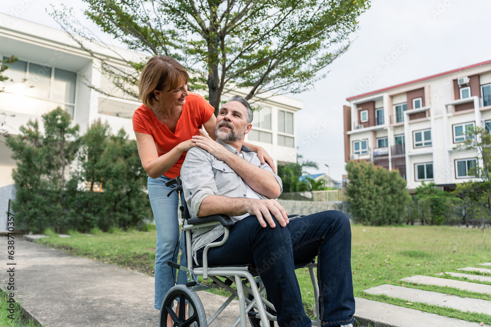 Caucasian senior woman support husband on wheelchair outdoor in garden. 