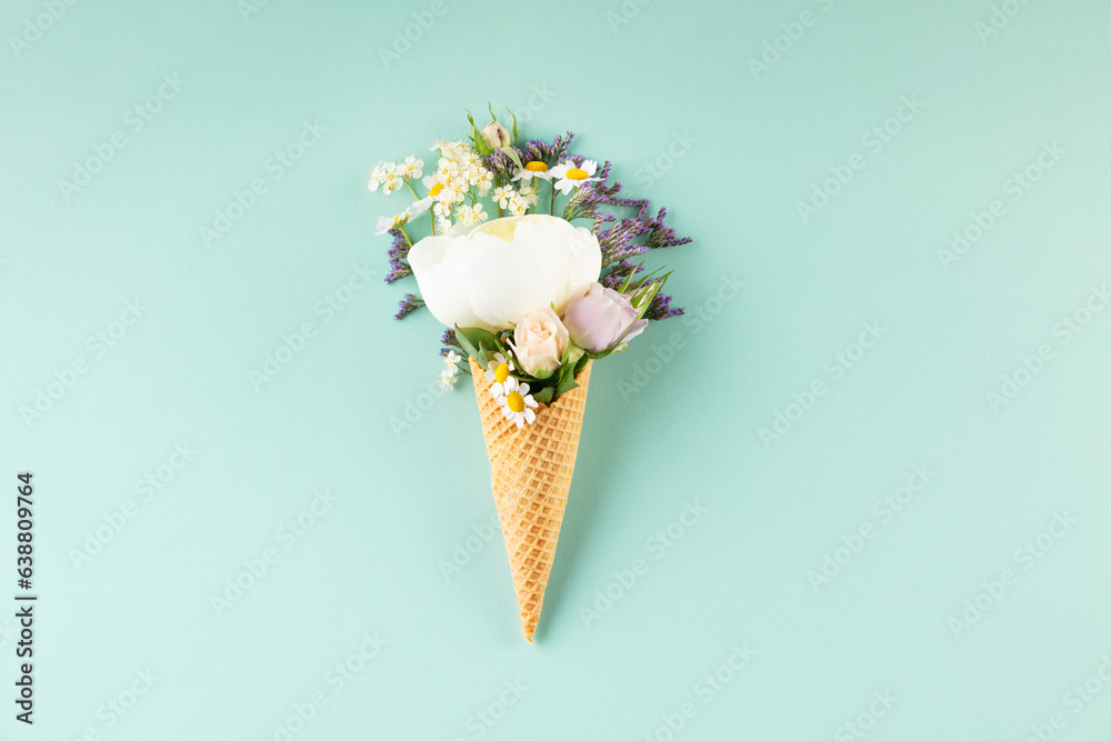 Flat-lay of waffle cone with flowers over pastel light blue background, top view