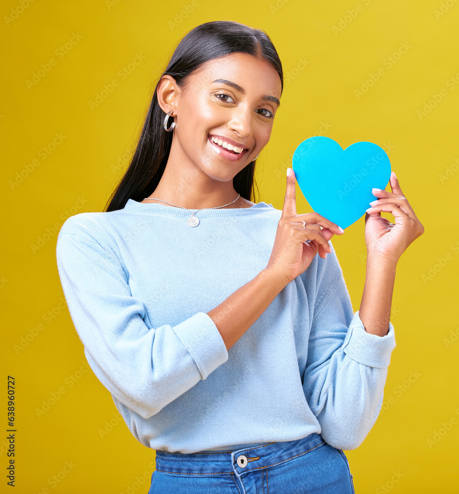 Portrait, donation and woman with blue heart in studio for help, hope or empathy on yellow backgroun