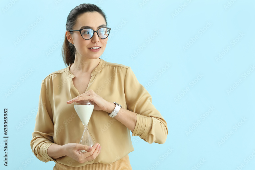 Young woman with wristwatch and hourglass on blue background