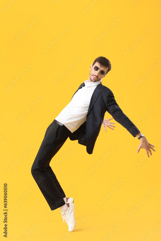 Young man in sunglasses dancing on yellow background