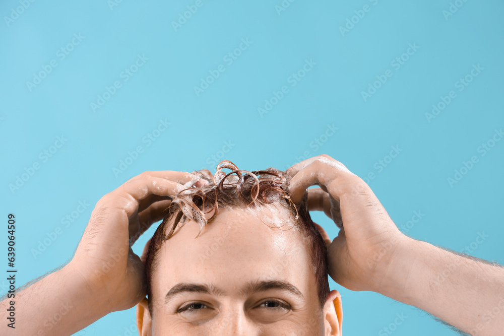 Young man washing hair against light blue background