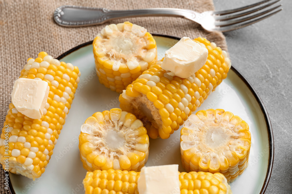 Plate of boiled corn cobs with butter on grey background