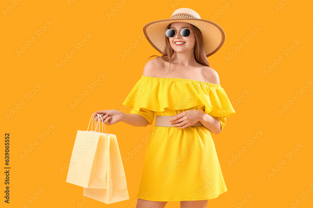 Pretty young woman with shopping bags on orange background