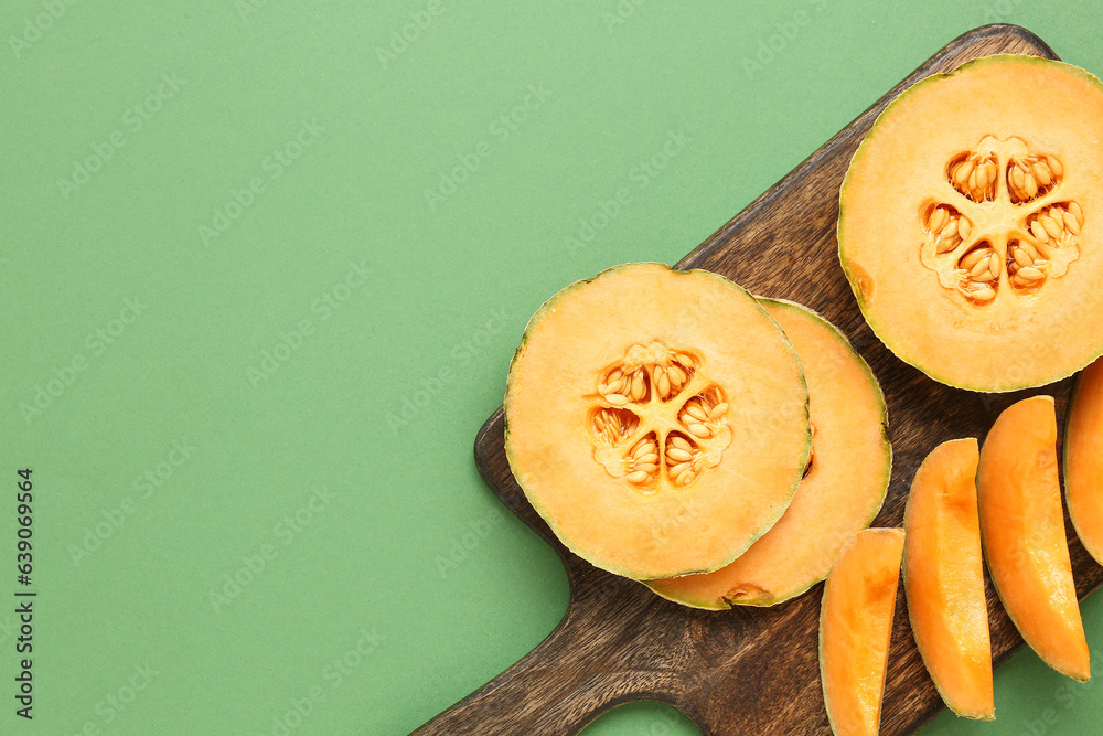 Wooden board with pieces of sweet melon on green background