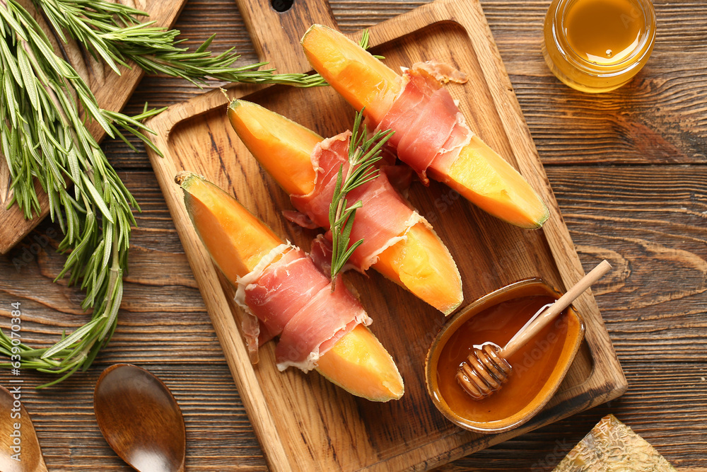 Board of tasty melon with prosciutto, rosemary and honey on wooden background