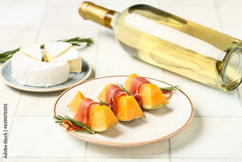 Plate of tasty melon with prosciutto, cheese and wine on light tile background