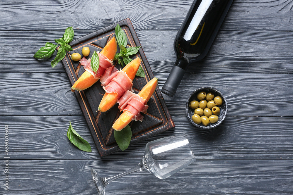 Tasty melon with prosciutto, green olives and bottle of wine on dark wooden background